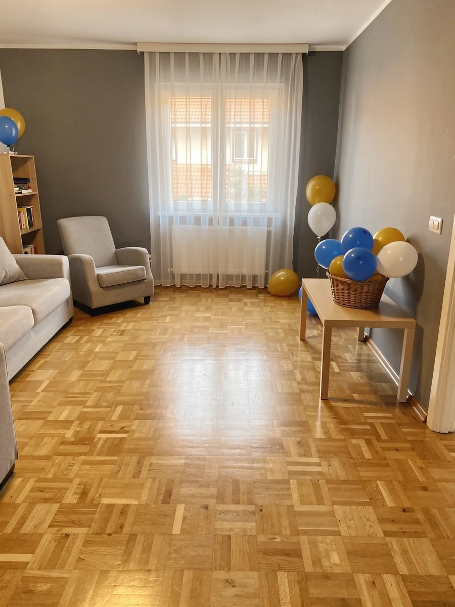 Prazan dnevni boravak s pomaknutim namještajem, košarom balona i niskim stolom uz zid